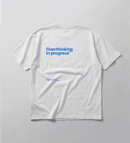 White t-shirt with blue text 'Overthinking in progress' on a light gray background