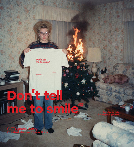 Person holding a 'Don't tell me to smile' shirt in a room with a burning Christmas tree and scattered items.